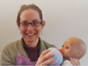 Screengrab of Emily with doll and knitted breast